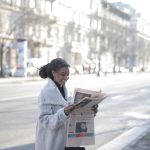 African American woman reading a newspaper on an urban street, enjoying a peaceful morning. — examplearticle